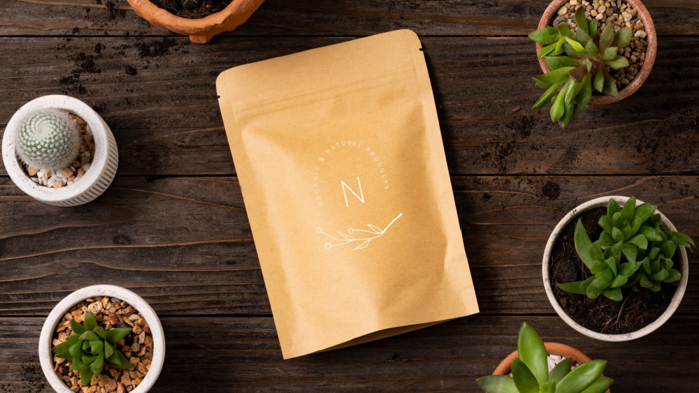 A kraft paper pouch with a minimalistic design, placed on a wooden table with small potted plants.