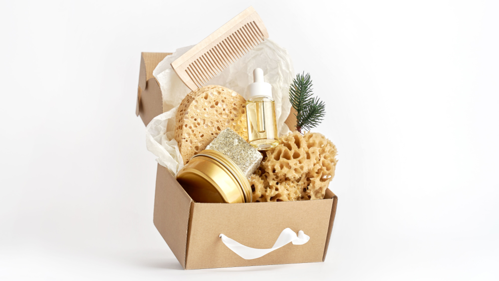 A cardboard box filled with eco-friendly products like a wooden comb, natural sponges, and glass containers.