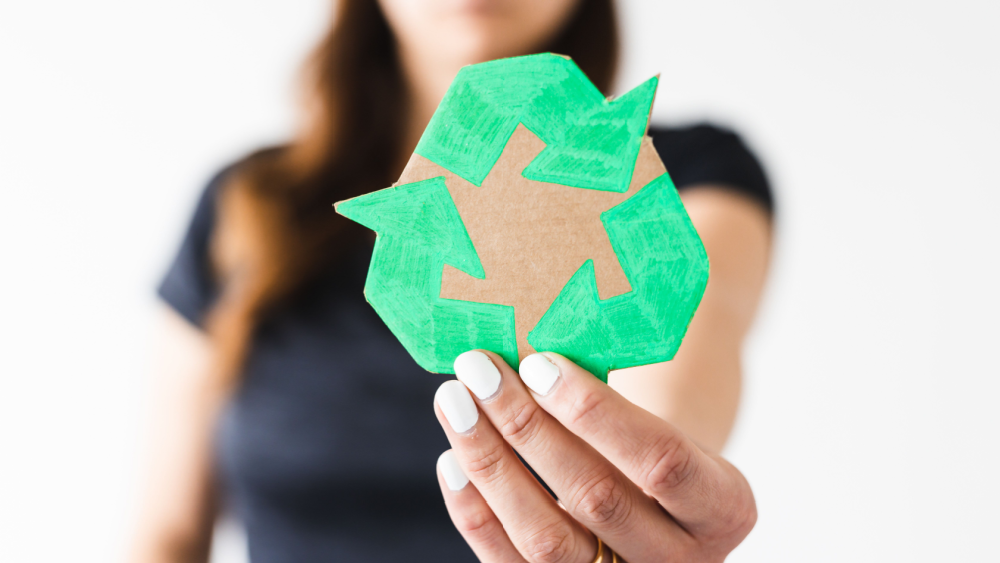 A woman holding a cardboard cutout of a recycling symbol.